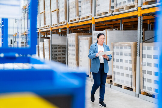 Businesswoman walks in the warehouse checking inventory on a tablet