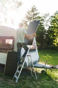 Man installing solar panel on camper roof at campsite