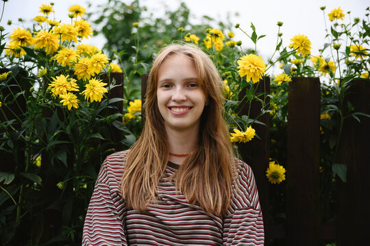 A smiling girl enjoys a summer day by a wooden fence with flower