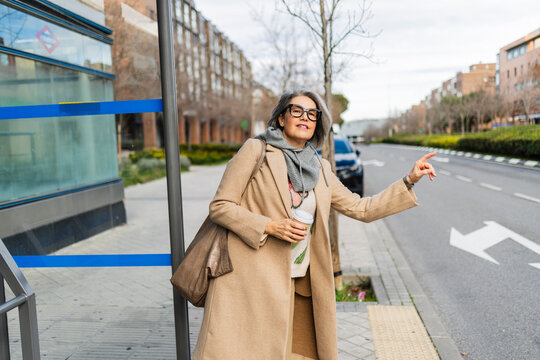 Mature woman waiting at bus stop with coffee in urban city setting