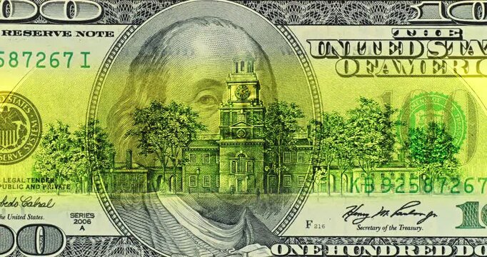 100 dollar bill under moving security scan. Benjamin Franklin portrait anchors colorful United States banknote artwork. Engraved details and national emblems form striking historic design.