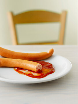 A broken sausage with ketchup lies abandoned on a white plate
