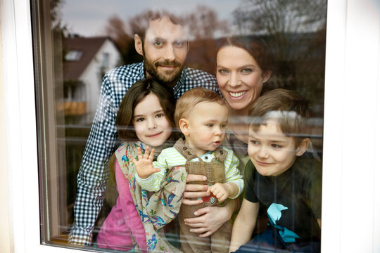 Happy family of five looking through window pane