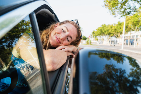 Happy woman relaxes her head on the car window
