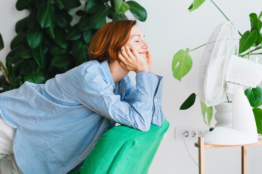 A smiling woman enjoys the cool breeze from an electric fan at home