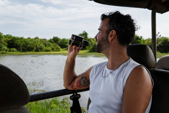 Man using binoculars on safari jeep by lake in Sigiriya Sri Lanka