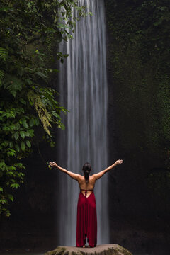 Tourist in red dress admires a jungle waterfall in Bali