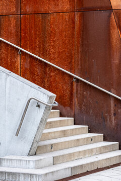 Modern staircase beside a rusted metal wall with handrail where architecture geometry shapes the urban exterior around the staircase and wall