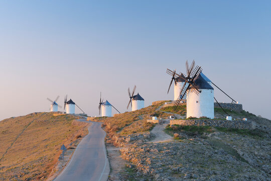 Traditional windmills stand along a rural road in Consuegra at dawn