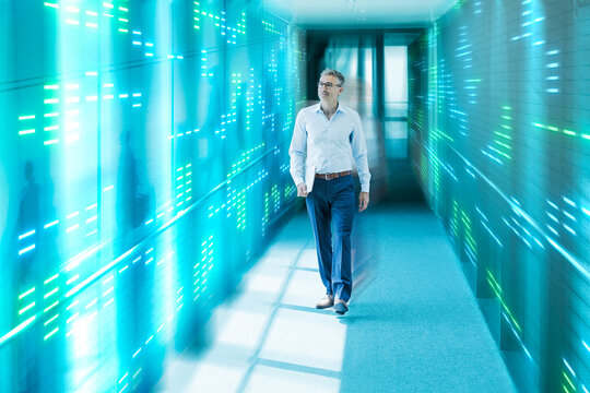 Businessman walks in a digital server corridor holding a laptop