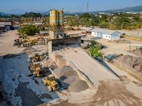 Aerial view of a concrete batching plant with tall silos, heavy construction machinery, and piles of aggregate in Semarang Regency, Central Java, Indonesia.