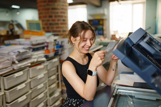 Smiling female operator reads a document at the office printer