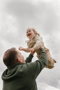 Happy father lifting his laughing baby daughter against the sky