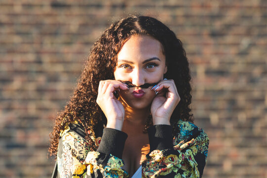 Portrait of young woman playing with her hair in front of brick wall