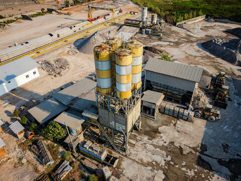 Aerial view of a concrete batching plant with tall yellow silos, heavy construction machinery, and piles of gravel in Semarang Regency, Central Java, Indonesia.