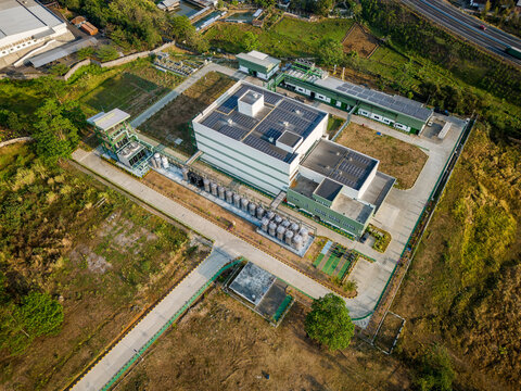 Aerial view of an industrial facility with solar panels on rooftops, large storage tanks, and a paved courtyard surrounded by green landscape in Semarang Regency, Central Java, Indonesia.
