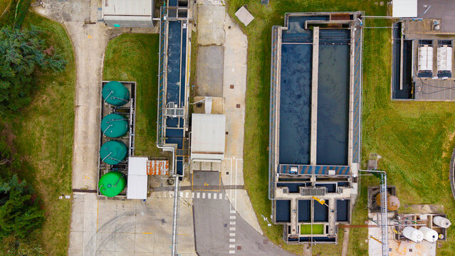 Aerial view of a wastewater treatment plant with circular green tanks and rectangular sedimentation basins surrounded by grassy areas in Rancate, Lombardia, Italy.