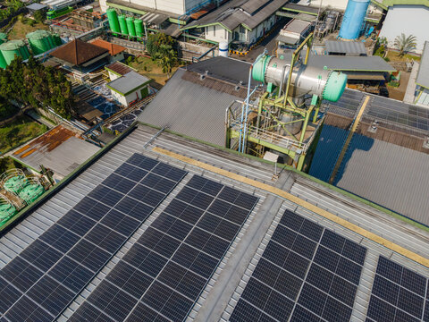 Aerial view of solar panels installed on a factory rooftop, featuring industrial machinery, storage tanks, and facility buildings in Banyumas Regency, Central Java, Indonesia.