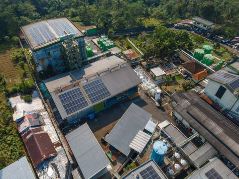 Aerial view of an industrial facility featuring solar panels on rooftops, storage tanks, and surrounding lush greenery in Banyumas Regency, Central Java, Indonesia.