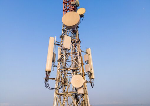 Aerial view of a telecommunications tower equipped with various antennas and satellite dishes against a clear blue sky in Cilongok, Central Java, Indonesia.