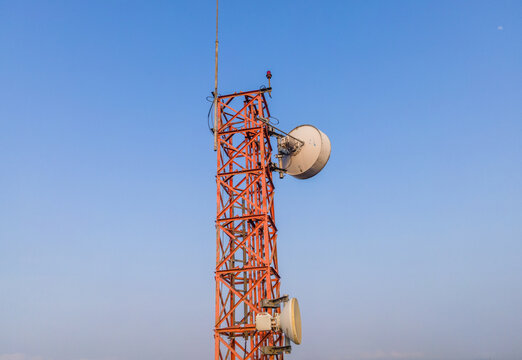 Aerial view of a red metal telecommunications tower with microwave dishes against a clear blue sky in Cilongok, Central Java, Indonesia.