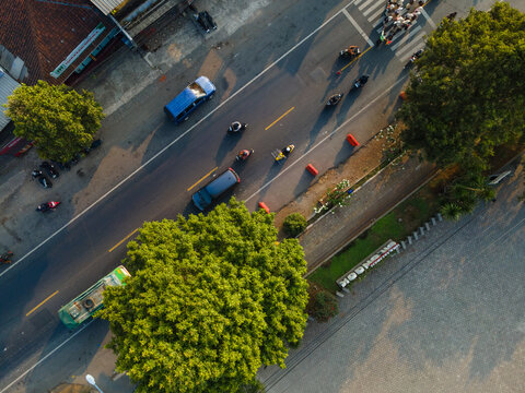 Aerial view of a road with cars and motorcycles driving past lush green trees and a roadside sign in Cilongok, Central Java, Indonesia.