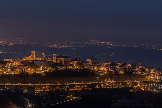 Aerial view of the illuminated town of Cingoli at night, featuring historic buildings, glowing streetlights, and a dark landscape in the background in Cingoli, Marche, Italy.