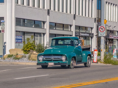 Calgary, AB, Canada. Oct 1, 2026. A classic teal vintage pickup truck driving on an urban street past city storefronts on a sunny day.