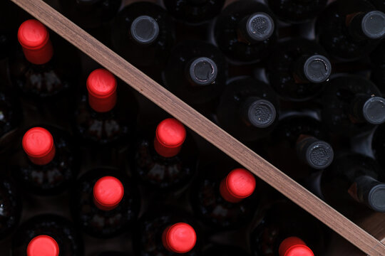 Top view shows dark bottles with bright red closures beside bottles with dark closures, separated diagonally by a wooden divider in storage