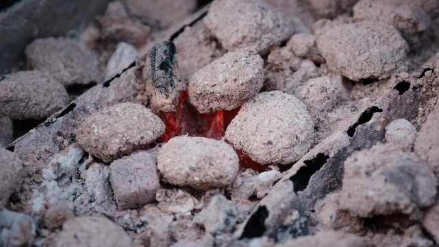 Close-up shot of glowing hot charcoal briquettes covered in ash in an outdoor barbecue grill.