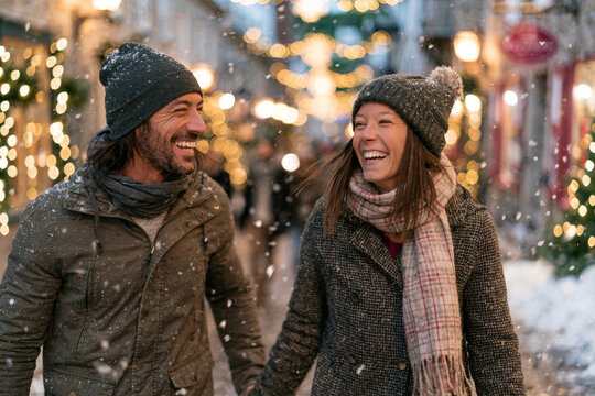 Smiling couple walking hand in hand through a charming snowy village decorated with warm holiday lights, fresh snowfall, cinematic natural lighting, , , , premium advertising style