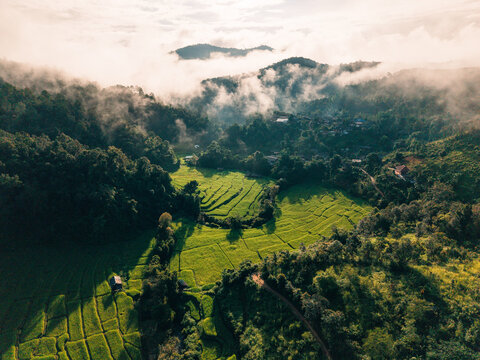 Aerial view of terraced rice fields in a valley surrounded by foggy mountains at sunrise in Southeast Asia.