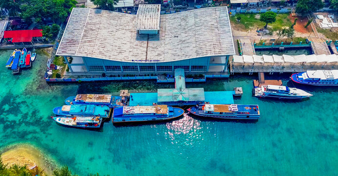 Aerial view of Dermaga Pulau Tidung pier extending into turquoise waters, surrounded by tropical islands and clear sky in South Kepulauan Seribu, Jakarta, Indonesia.