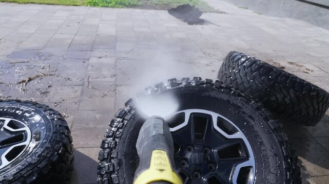 High-pressure water jets clean rugged tires. Wheels lie on concrete, ready for thorough cleaning. Steam sprays from nozzle, targeting dirt and grime. Utility tools work fast, leaving surfaces shiny
