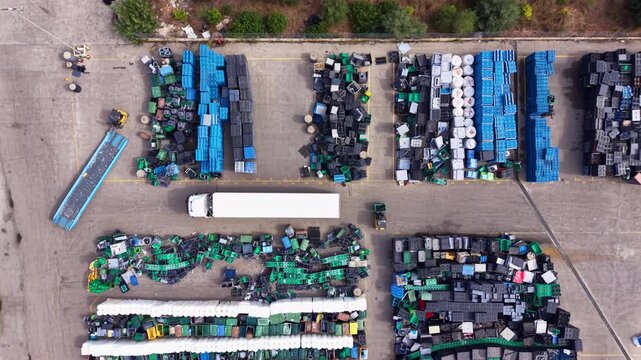 Top-down view of large outdoor plastic recycling yard with sorted colored crates, containers, pallets and waste materials arranged in rows with a truck on site