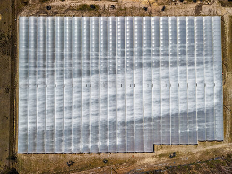 Aerial view of a large greenhouse complex with multiple parallel rows of translucent plastic tunnels, surrounded by dry earth and sparse vegetation in The Summit, Queensland, Australia.