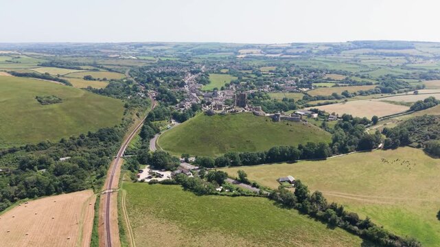 Corfe Castle Isle of Purbeck Dorset, England, high forward drone footage along Swanage to Corfe railway towards the castle and village with views of the surrounding countryside on bright sunny day