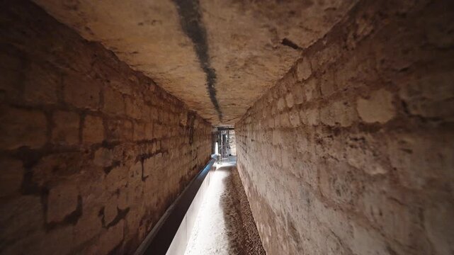 Long stone corridor in the Paris catacombs with a lit gravel path receding into a distant doorway.