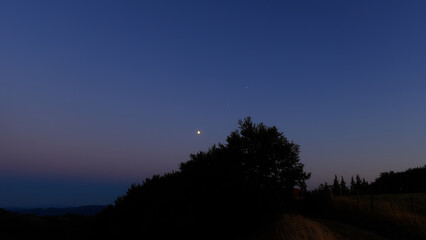 Moon on a twilight sky with stars, planets and landscape mountain silhouettes. © astrosystem