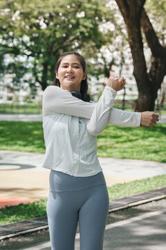 Asian woman stretching arms in sunny park for outdoor fitness warmup routine