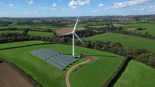 Liskeard, Cornwall, England: DRONE VIEWS: 1. Wind turbine with solar panel "farm"; 2. The town of Liskeard in the b/g. Wind power is an integral part of the UK government's strategy for net zero.