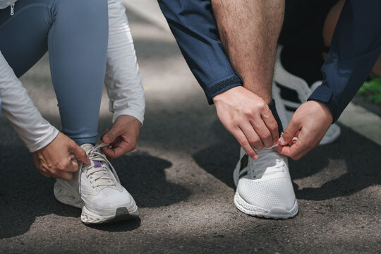 Athletes tying running shoes on pavement for fitness training and outdoor exercise