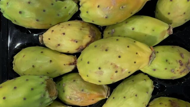 Top view of group of fresh green and orange prickly pears (Opuntia ficus-indica) piled up on a retail display. Tracking shot of healthy tropical and Mediterranean cactus fruits rich in vitamins