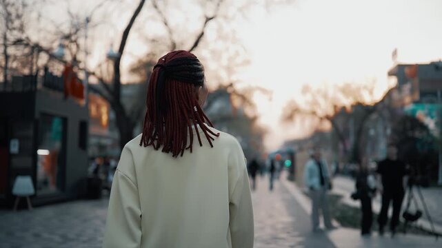 Woman smiling walking city street at sunset with braid and sweatshirt