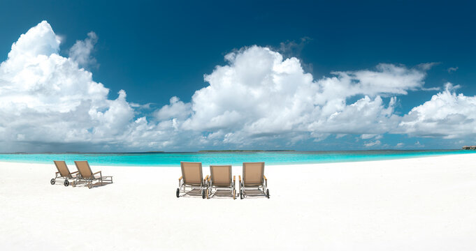 Panoramic view of empty sun loungers on white sand beach facing turquoise ocean under blue sky with fluffy clouds