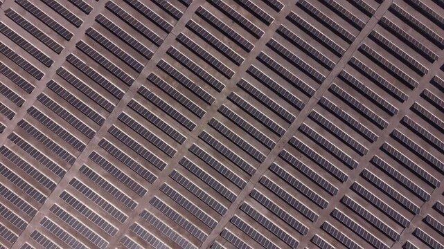 Top-down view of a massive solar panel array arranged in diagonal rows across arid terrain, forming geometric patterns that showcase large-scale renewable energy infrastructure