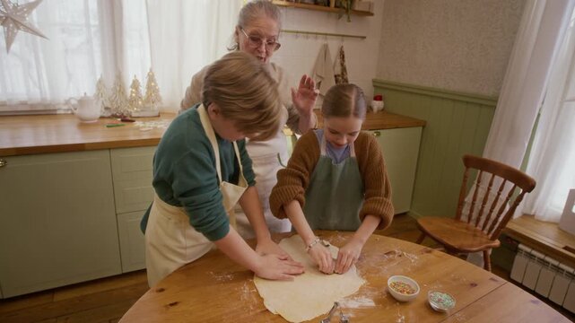 Senior Caucasian woman guiding Caucasian boy and girl cutting cookie dough. High angle arc view ideal for holiday cooking campaigns and intergenerational lifestyle projects
