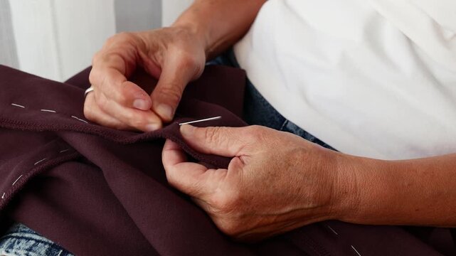 Senior woman hand stitching garment with needle and thread. Close-up of clothing alteration and sewing process at home.