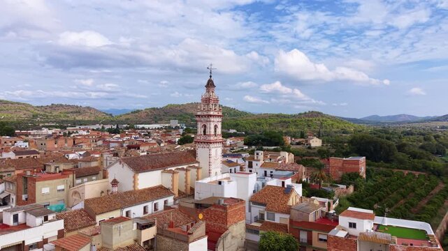 Elevated view of Estivella village in Camp de Morvedre, Valencia, Spain, featuring the ornate parish church bell tower rising above traditional terracotta rooftops with Serra Calderona mountains behin