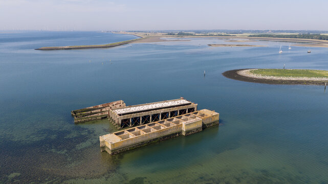 Aerial view of Caissons Inlaag Schelphoek, historic concrete structures submerged in coastal waters, surrounded by calm sea and tidal flats in Serooskerke Schouwen, Zeeland, Netherlands.
